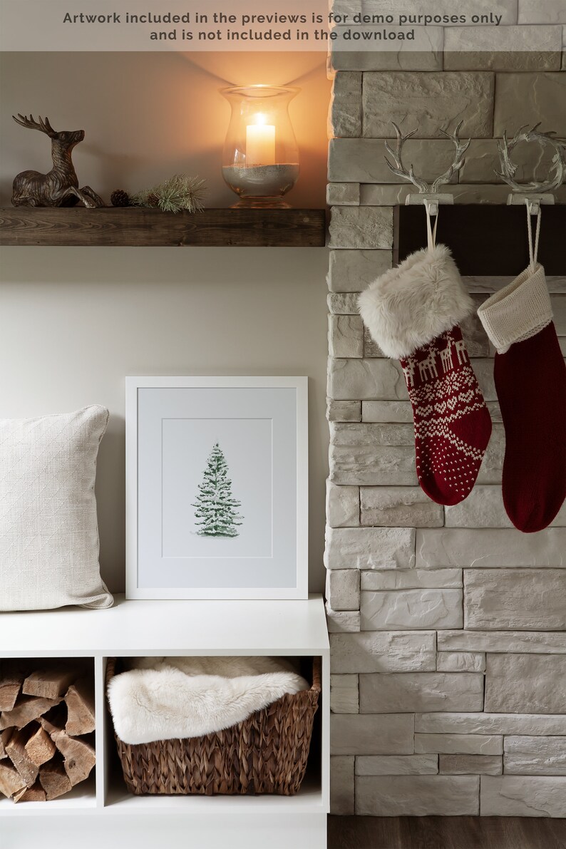 May include: A white shelf with a wooden top, a framed print of a green Christmas tree, a white faux fur throw in a wicker basket, and a stack of firewood in a cubby below. Two red and white Christmas stockings hang on a brick fireplace.