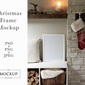 May include: A white picture frame mockup with a white mount, sitting on a white shelf with a white faux fur throw in a wicker basket. The shelf is part of a white bookcase with a wood-burning fireplace in the background. There are two red and white Christmas stockings hanging on the fireplace mantle.
