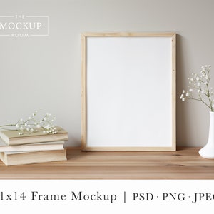 May include: A 11x14 inch wood frame mockup with a white mount and a white background. The frame is sitting on a wooden table with a stack of books and a vase of white flowers.