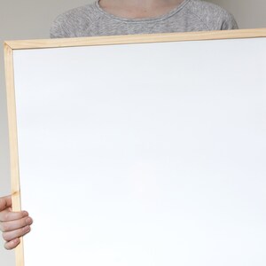 May include: A person holding a white framed whiteboard.