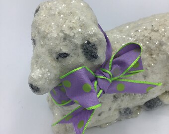 May include: A white, glitter-covered dog figurine with black spots. The dog wears a purple ribbon with green polka dots and green trim. The figurine is a decorative item.