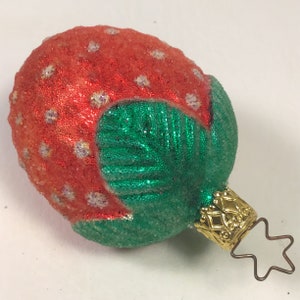 May include: A red and green glass Christmas bauble shaped like a strawberry with a gold star topper.