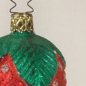 May include: A red and green Christmas bauble shaped like a strawberry. The bauble is covered in small beads and has a gold top.