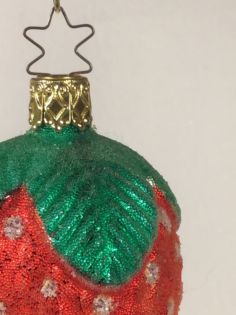 May include: A red and green Christmas bauble shaped like a strawberry. The bauble is covered in small beads and has a gold top.