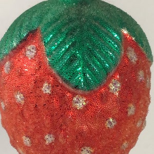 May include: A red and green Christmas bauble shaped like a strawberry. The bauble is covered in small, sparkly beads.
