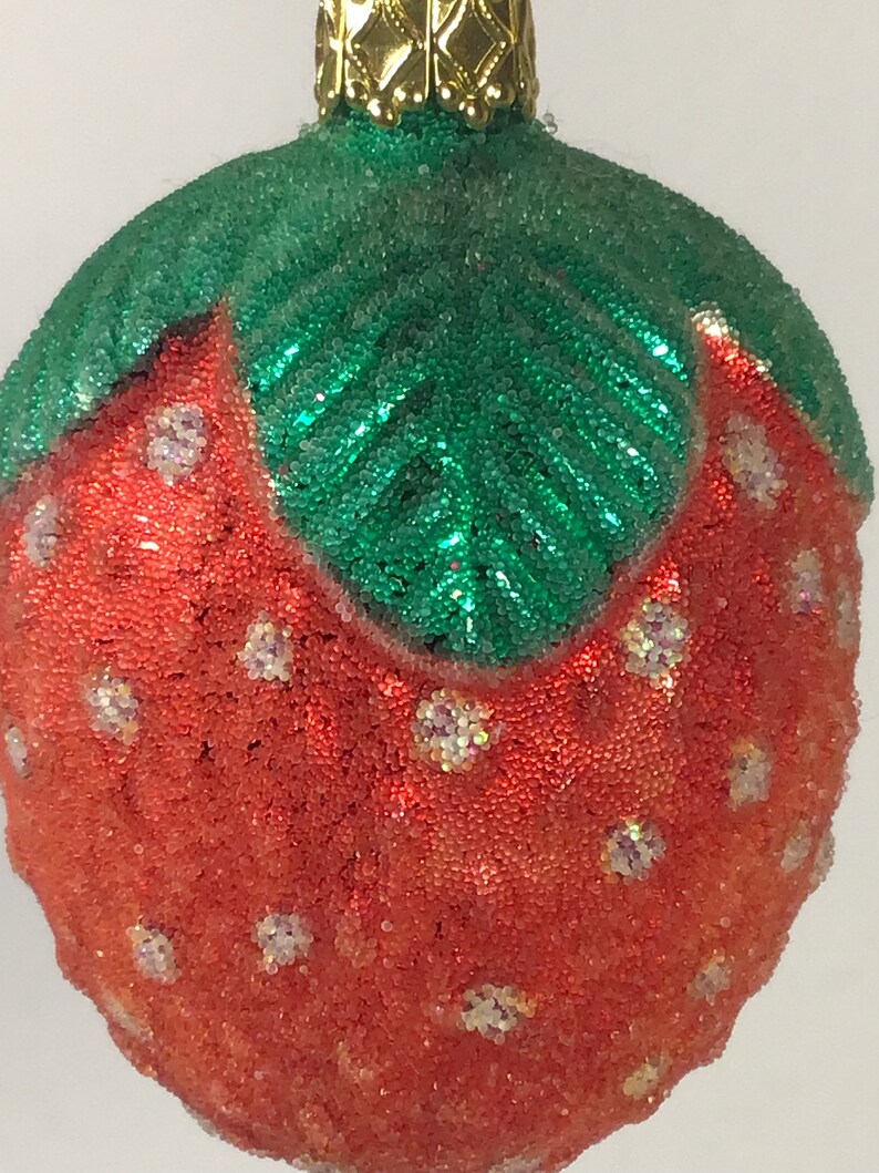 May include: A red and green Christmas bauble shaped like a strawberry. The bauble is covered in small, sparkly beads.