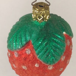 May include: A red and green glass Christmas bauble shaped like a strawberry. The bauble is covered in glitter and has a gold top.
