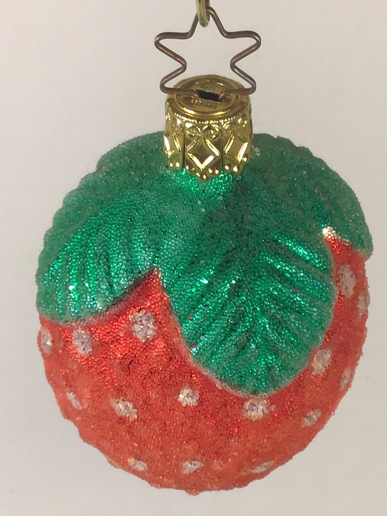 May include: A red and green glass Christmas bauble shaped like a strawberry. The bauble is covered in glitter and has a gold top.