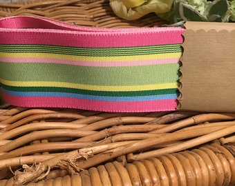 May include: Pink and green striped ribbon with a light blue stripe. The ribbon is on a wicker surface.