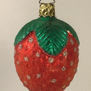 May include: A red and green glass Christmas bauble shaped like a strawberry. The strawberry has white glitter accents and a green leaf on top.