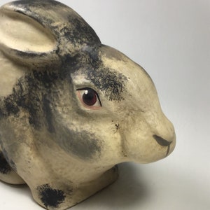 May include: A hand-painted ceramic rabbit figurine with black and white markings and red eyes. The rabbit is in a sitting position with its head tilted to the side.