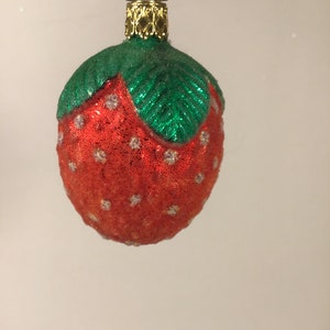 May include: A red and green glass Christmas bauble shaped like a strawberry. The strawberry has white dots on it.