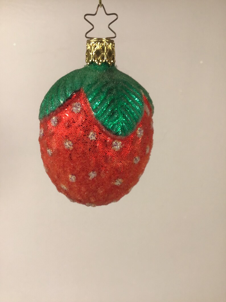 May include: A red and green glass Christmas bauble shaped like a strawberry. The strawberry has white dots on it.