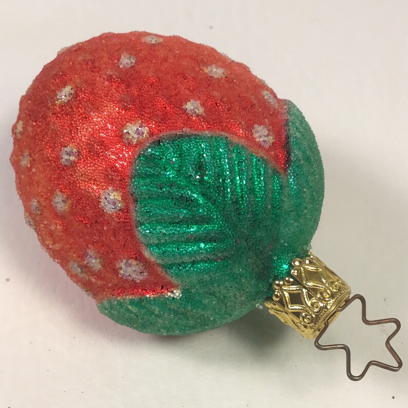 May include: A red and green glass Christmas bauble shaped like a strawberry with a gold star topper.