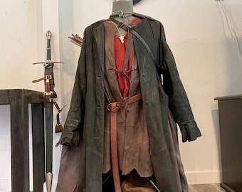Könnte beinhalten: Ein brauner Ledermantel mit einem roten Hemd und einer braunen Lederhose. Das Outfit ist auf einem Mannequin mit einem Schwert und Pfeilen im Hintergrund. Das Schild darüber lautet "The Prancing Pony."