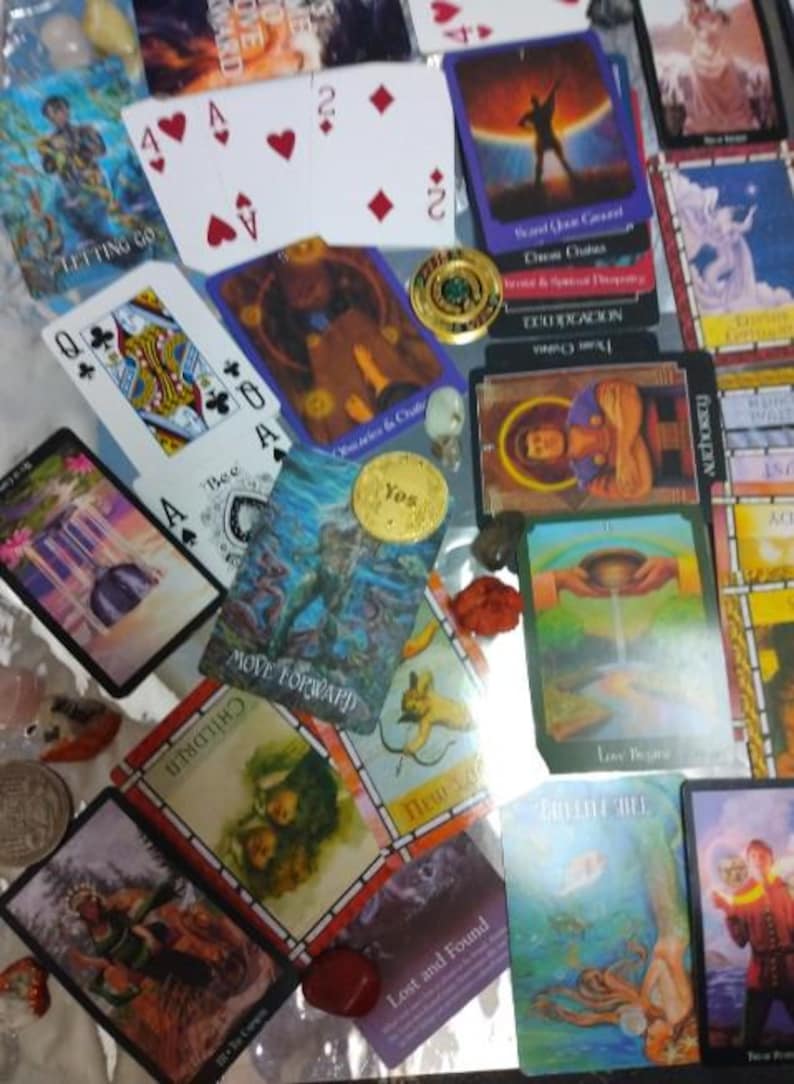 May include: A collection of tarot cards, playing cards, and small metal coins scattered together. The cards feature various colourful illustrations, including figures, landscapes, and text like 'Move Forward', 'Children', and 'Love Begins'.