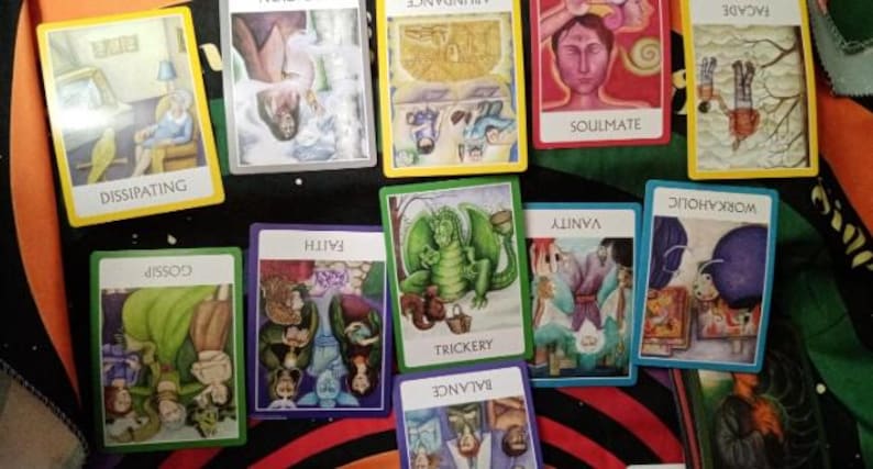 May include: A collection of rectangular oracle cards with colourful illustrations and white borders. The cards feature various titles including Dissipating, Abundance, Soulmate, Facade, Gossip, Faith, Trickery, Vanity, Workaholic, and Balance.