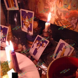May include: A collection of tarot cards featuring purple and white illustrations, arranged alongside several lit candles in various colours including white and purple. The scene includes a red bowl and scattered stones, with the text PSYCHIC INSIGNIA visible.