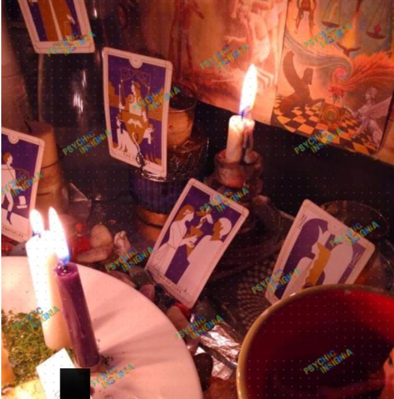 May include: A collection of tarot cards featuring purple and white illustrations, arranged alongside several lit candles in various colours including white and purple. The scene includes a red bowl and scattered stones, with the text PSYCHIC INSIGNIA visible.