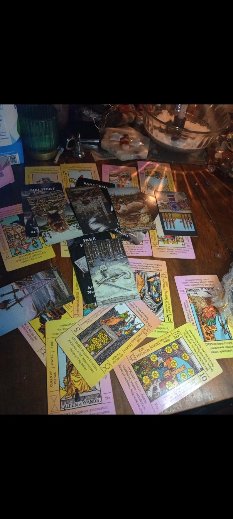 May include: A collection of tarot cards spread across a surface, featuring various illustrations including a wolf, swords, and pentacles. The cards display text such as Girl Fight, Fake, Queen of Wands, and King of Wands, with colourful imagery.