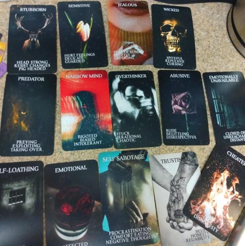 May include: A collection of rectangular oracle cards featuring dark, evocative imagery and text labels. Each card displays a specific theme such as Stubborn, Sensitive, Jealous, Wicked, Predator, Narrow Mind, Overthinker, Abusive, Emotionally Unavailable, Self-Sabotage, Trusting, and Cheater, accompanied by descriptive keywords.