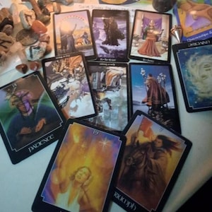 May include: A collection of tarot cards spread out, including cards labelled Patience, Triumph, and Universe. The cards feature various illustrations of figures, landscapes, and celestial imagery in a mix of upright and inverted orientations.