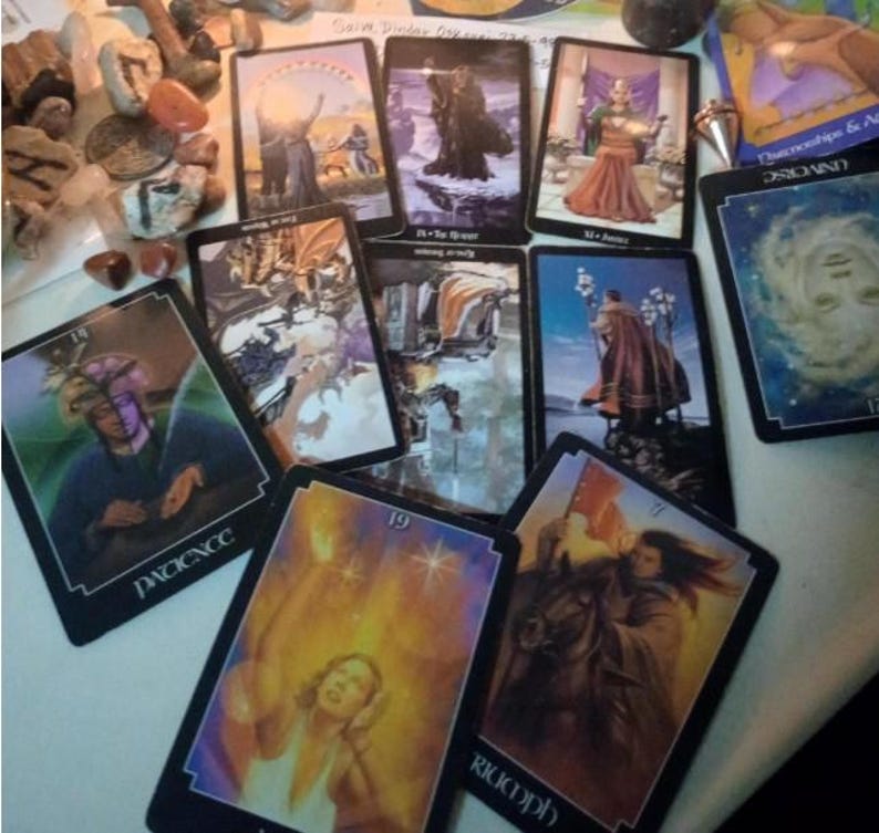 May include: A collection of tarot cards spread out, including cards labelled Patience, Triumph, and Universe. The cards feature various illustrations of figures, landscapes, and celestial imagery in a mix of upright and inverted orientations.