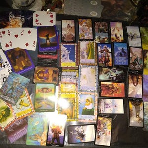 May include: A collection of numerous tarot cards and playing cards spread across a surface. The cards feature various colourful illustrations, figures, and text labels such as Letting Go, Authority, Focus, Wish Wisely, and Hope, alongside standard playing card suits.