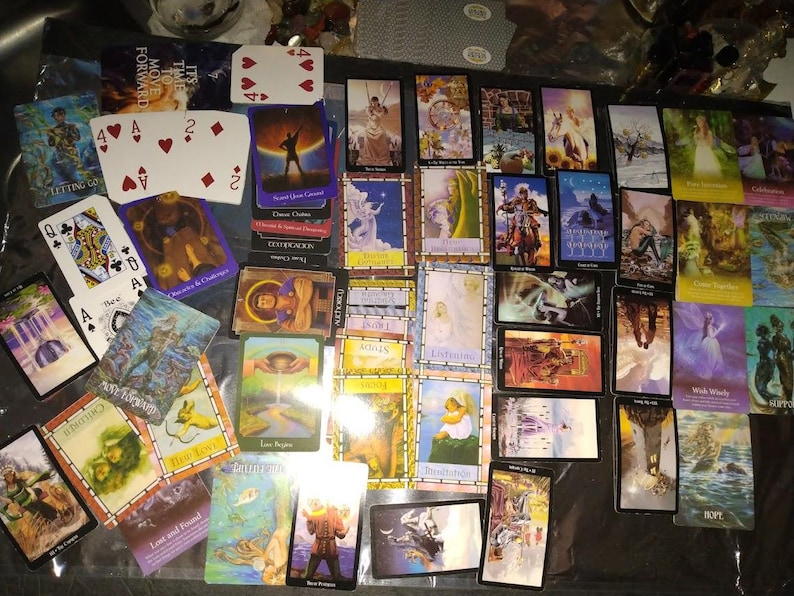 May include: A collection of numerous tarot cards and playing cards spread across a surface. The cards feature various colourful illustrations, figures, and text labels such as Letting Go, Authority, Focus, Wish Wisely, and Hope, alongside standard playing card suits.