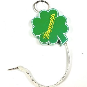 May include: A green shamrock-shaped tape measure with the text "Fitzgeralds Casino/Hotel - Reno" in yellow. The tape measure is white with black measurement markings and a metal end piece. A silver key ring is attached.
