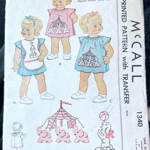 May include: Vintage McCall's sewing pattern for toddlers' one-piece apron-dress and bib. The pattern features illustrations of children's clothing with circus-themed designs, including elephants and a circus tent. The pattern is labeled "1340" and is suitable for children aged 1-2-3 years.