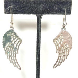 K&ouml;nnte beinhalten: Ein Paar silberfarbene Ohrringe in Fl&uuml;gelform. Jeder Ohrring hat ein detailliertes Fl&uuml;geldesign mit strukturierter Oberfl&auml;che und durchbrochenen Details. Die Ohrringe h&auml;ngen an einem einfachen Haken.