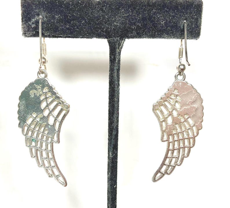 K&ouml;nnte beinhalten: Ein Paar silberfarbene Ohrringe in Fl&uuml;gelform. Jeder Ohrring hat ein detailliertes Fl&uuml;geldesign mit strukturierter Oberfl&auml;che und durchbrochenen Details. Die Ohrringe h&auml;ngen an einem einfachen Haken.