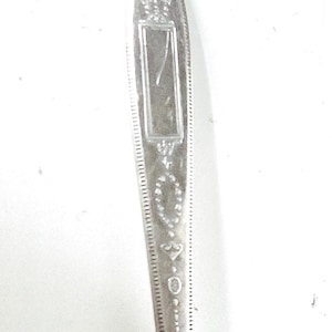 May include: Close-up of a silver spoon with ornate detailing. The spoon's handle features a rectangular design and decorative patterns. The number "32.0" is visible on the handle. The spoon is against a white background.