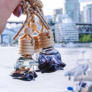 May include: Three glass car air fresheners with a rose-shaped design. The fresheners are filled with a dark liquid and have a wooden top with a gold string attached.