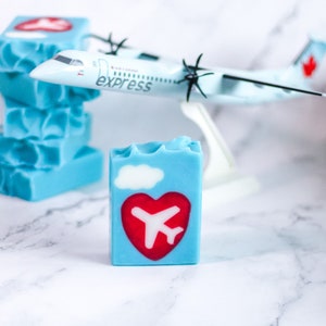Puede incluir: Un modelo de avión azul y blanco con las palabras "Air Canada Express" en el lateral. El modelo está sentado encima de una pila de barras de jabón azules con un corazón rojo y un diseño de avión.