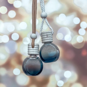 May include: Two small, round, blue glass bottles with silver caps hanging from white and brown cords. The bottles are hanging against a blurry background of white and gold lights.