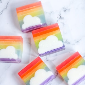 May include: Five rainbow-coloured soap bars with a white cloud design. Each bar has a different colour combination of red, orange, yellow, green, blue, and purple.