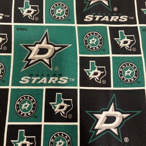May include: Fabric with a repeating pattern featuring the Dallas Stars logo in white, silver, and green. The design includes the team's star logo, the word "STARS", and the Texas outline with the team logo. The background alternates between black and green squares.