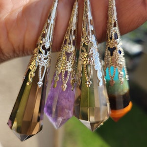May include: Four silver-toned pendants with faceted crystal points. Each pendant has a unique crystal color: smoky brown, purple, clear, and a mix of turquoise, green, and orange. The pendants are suspended from a silver chain.