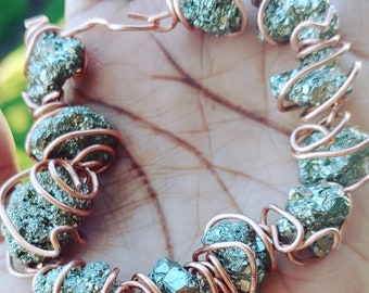 May include: A handmade bracelet featuring rough-cut pyrite stones wrapped in copper wire. The pyrite stones have a metallic, shimmering appearance, and the copper wire is intricately coiled around each stone, creating a unique and earthy design.