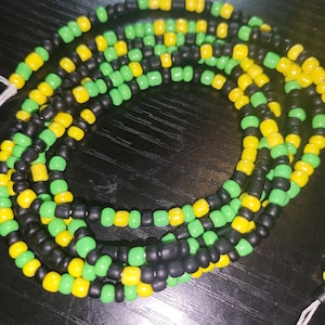 May include: Strands of colorful waist beads in black, yellow, and green. The beads are small and round, strung together to form multiple strands. The beads are arranged in a layered pattern, creating a visually appealing accessory.