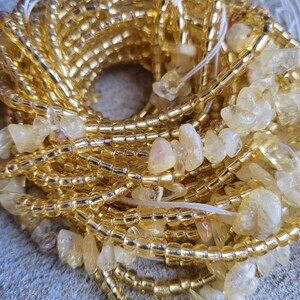 May include: A close-up of a golden beaded bracelet with small, clear, faceted stones. The bracelet is made of multiple strands of beads and is wrapped around itself.