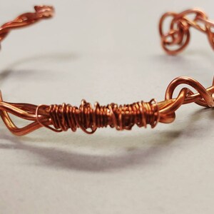 May include: A copper wire bracelet with a twisted and woven design.