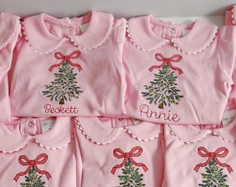 Puede incluir: Una colección de camisas de manga larga de color rosa claro con cuellos Peter Pan festoneados. Cada camisa presenta un árbol de Navidad bordado con un lazo rojo y un nombre personalizado en letra roja: Beckett, Annie, Greer, Parker y Scottie.