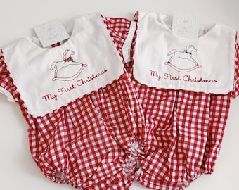 Pode incluir: Dois macacões de bolha em xadrez vichy vermelho e branco com gola de babador branca. Cada gola é bordada com um cavalo de balanço e o texto My First Christmas em fio vermelho. Os macacões têm mangas curtas e pernas franzidas.