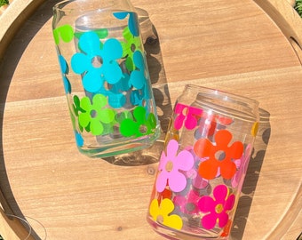 May include: Two glass tumblers with colourful flower designs. The tumbler on the left has blue, green, and white flowers. The tumbler on the right has pink, orange, and yellow flowers.