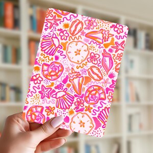 May include: A rectangular card featuring a vibrant pattern of seashells, starfish, and floral elements in shades of pink, orange, and white. The design is set against a white background, creating a summery and beach-themed aesthetic.