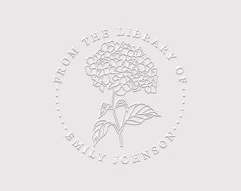 May include: A circular embosser design featuring a central hydrangea flower illustration. The text FROM THE LIBRARY OF is arched across the top, and the name EMILY JOHNSON is arched across the bottom, all rendered in a white embossed effect.