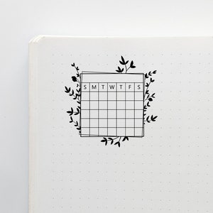 May include: A black and white weekly calendar planner with a floral design. The calendar has the days of the week labeled S, M, T, W, T, F, S.